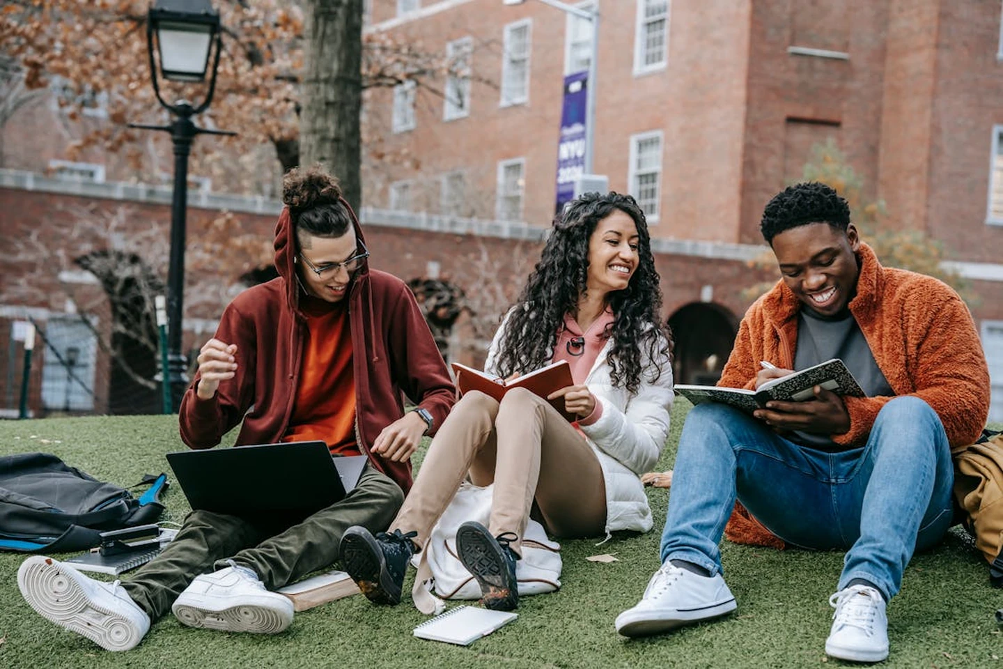 Three students studying together on a college campus lawn.